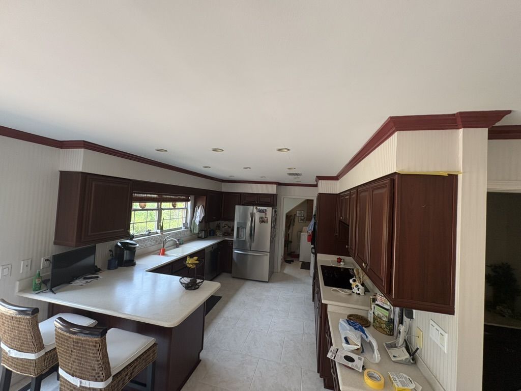 Kitchen before painting, with striped walls and dark red crown molding above dark wood cabinets